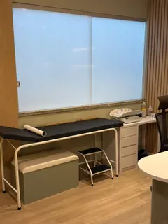 Consultório de pediatria, com maca, balança de bebê e régua de crescimento.